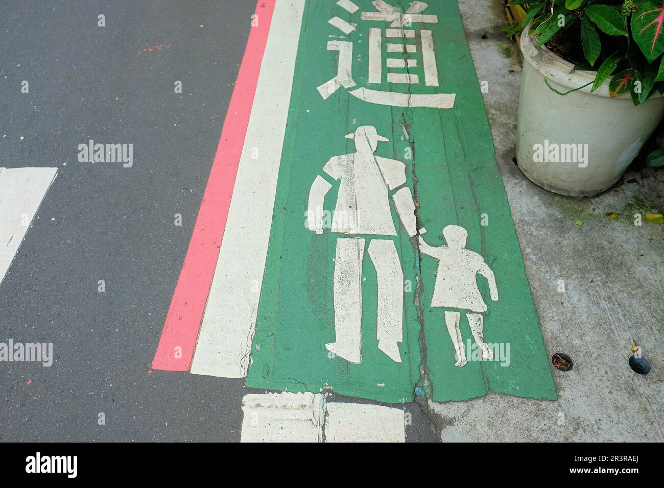 Sagoma bianca di un uomo che tiene la mano di un bambino su un sentiero verde designato sulla strada per pedoni e traffico pedonale; Taipei, Taiwan. Foto Stock