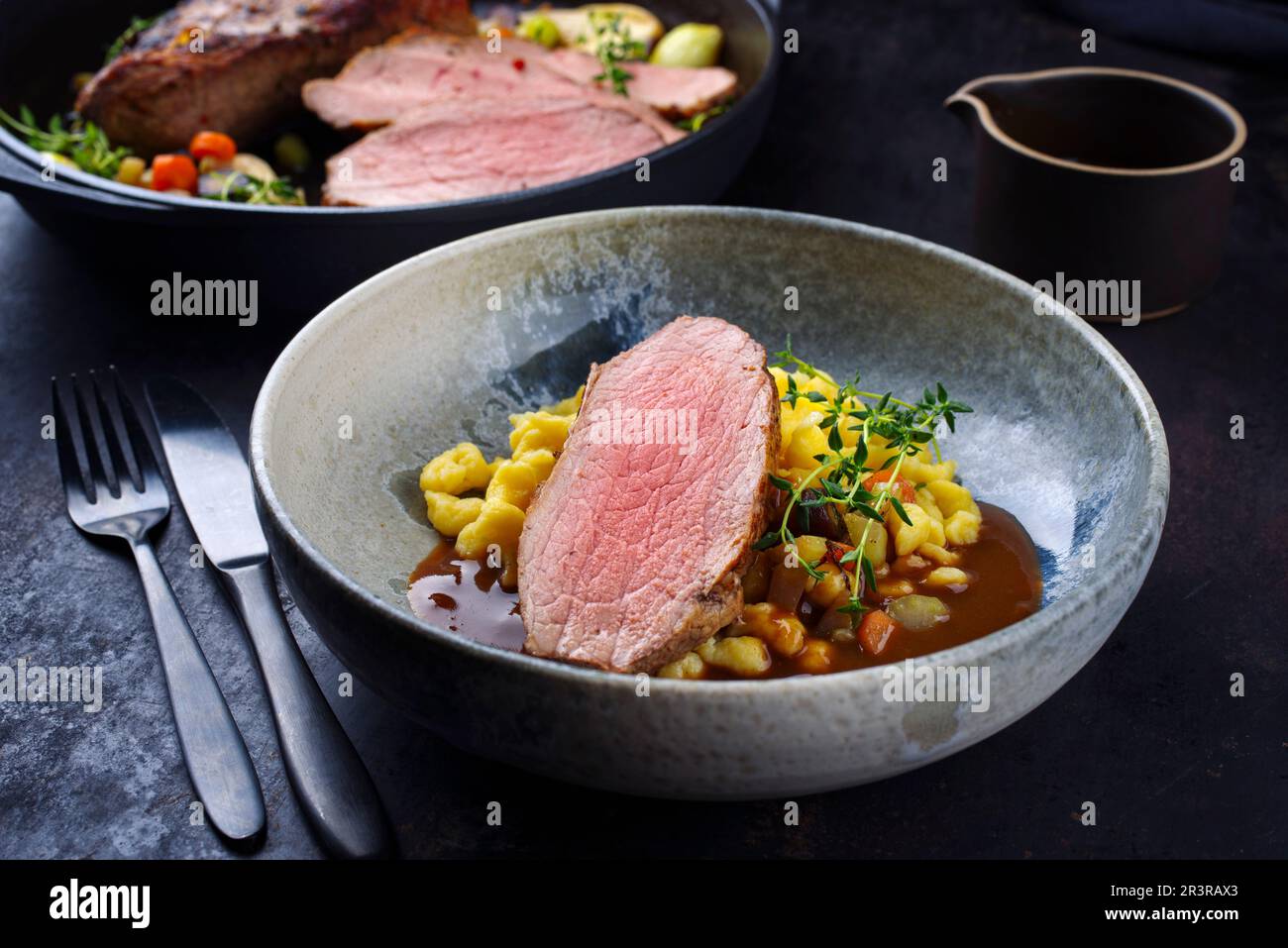 Fettine di vitello arrosto Tafelspitz con spaetzle svevo servite con salsa di birra scura come primo piano in una ciotola e una pentola di design Foto Stock