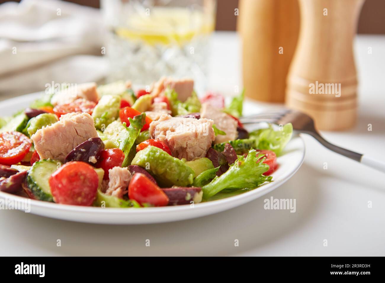 Insalata con tonno, lattuga, cetrioli, pomodori, olive e avocado in piatto bianco sul tavolo Foto Stock