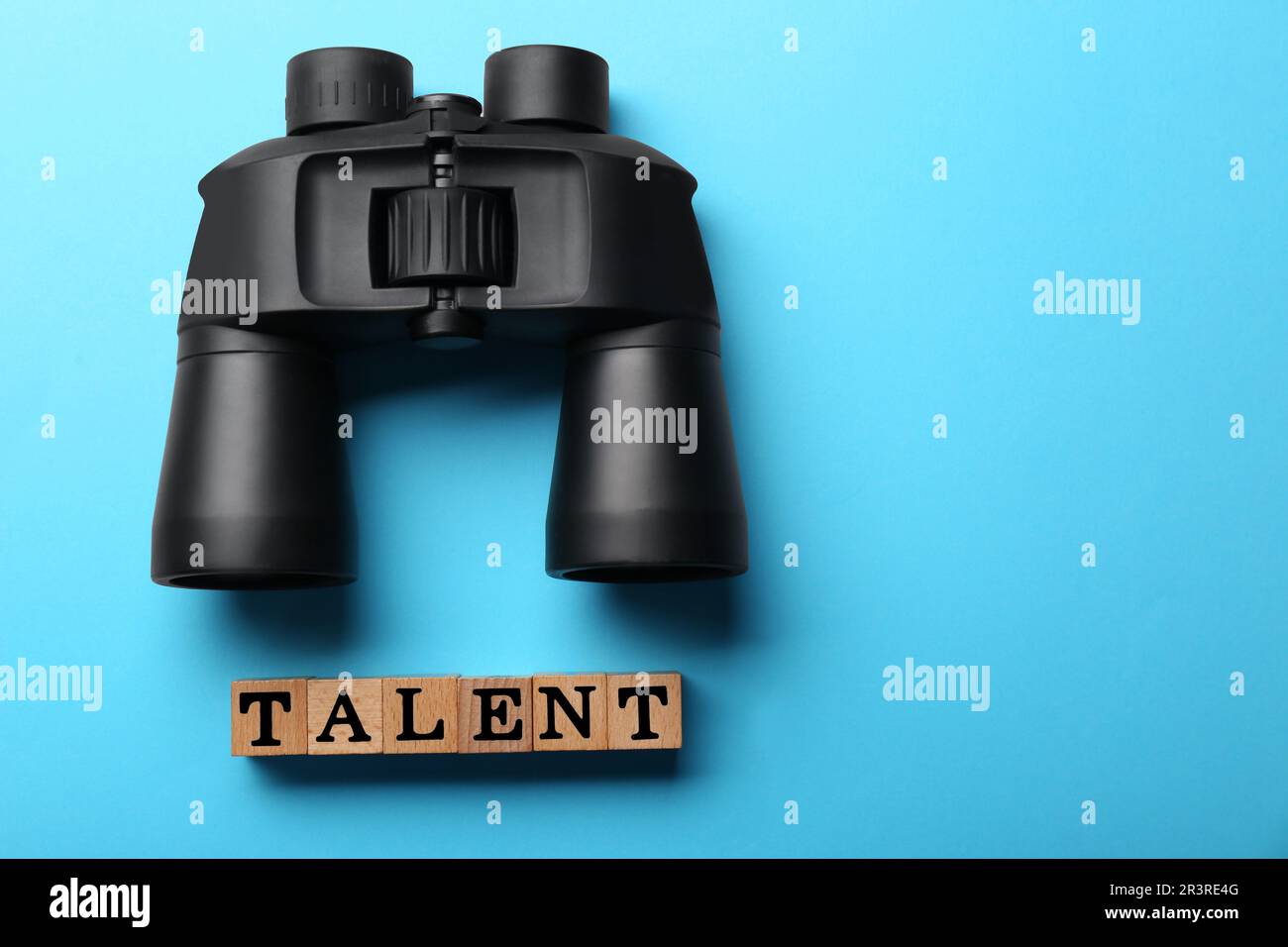 Concetto di reclutamento e assunzione. Talent parola fatto di cubetti di legno e binocolo su sfondo azzurro, piatto. Spazio per il testo Foto Stock