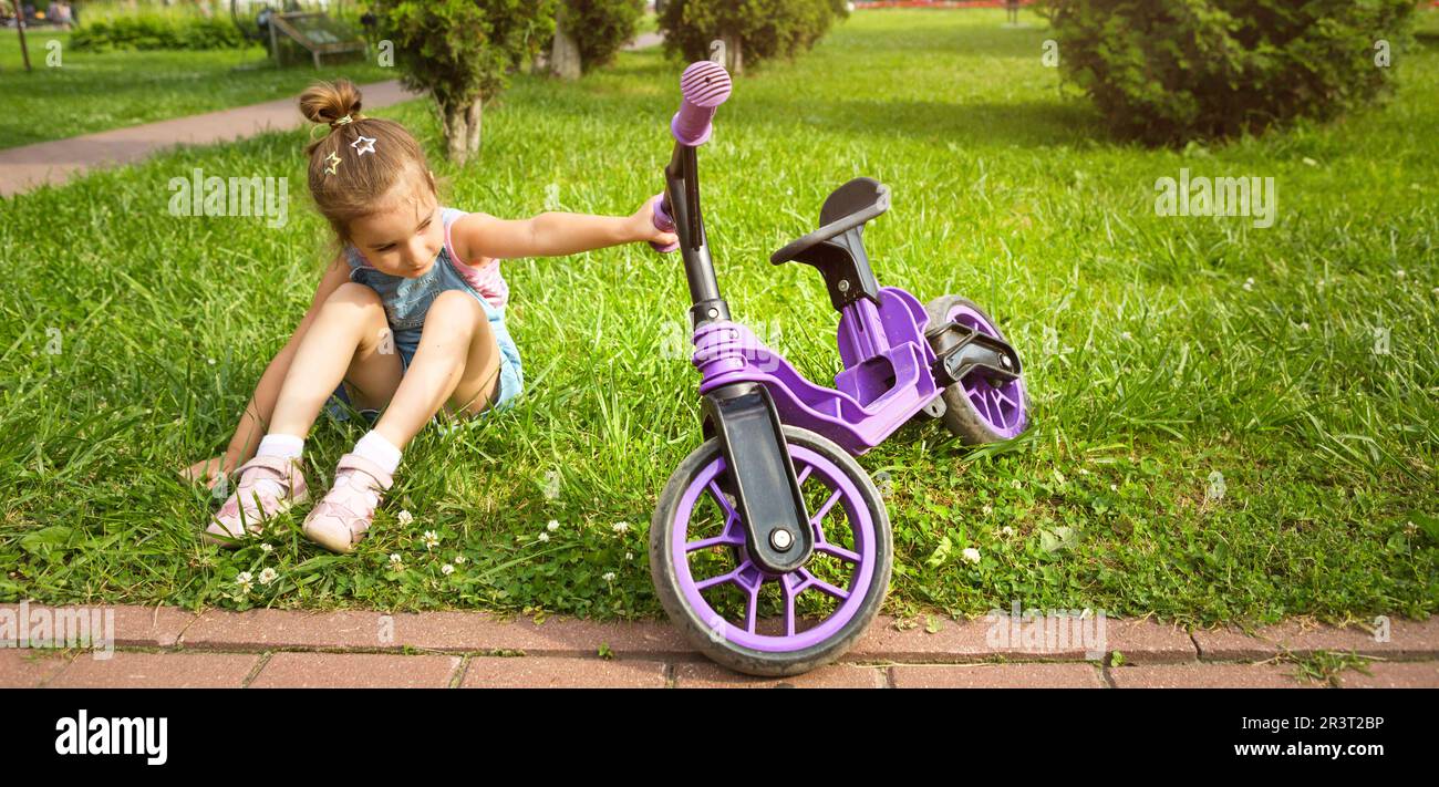 Ragazza allegra seduta riposata sull'erba in un parco vicino alla bici da corsa viola in estate. Animazione attiva per bambini Foto Stock