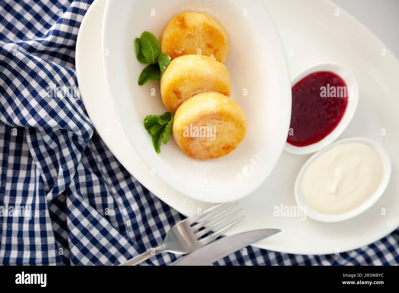 Frittelle di formaggio ricotta rotonda in un piatto bianco su sfondo blu. Cibo prima colazione. Cibo sano. Salsa di panna acida e menta. Primo piano vista dall'alto. Pasto dessert. Frittelle di ricotta al formaggio ricotta. Foto Stock