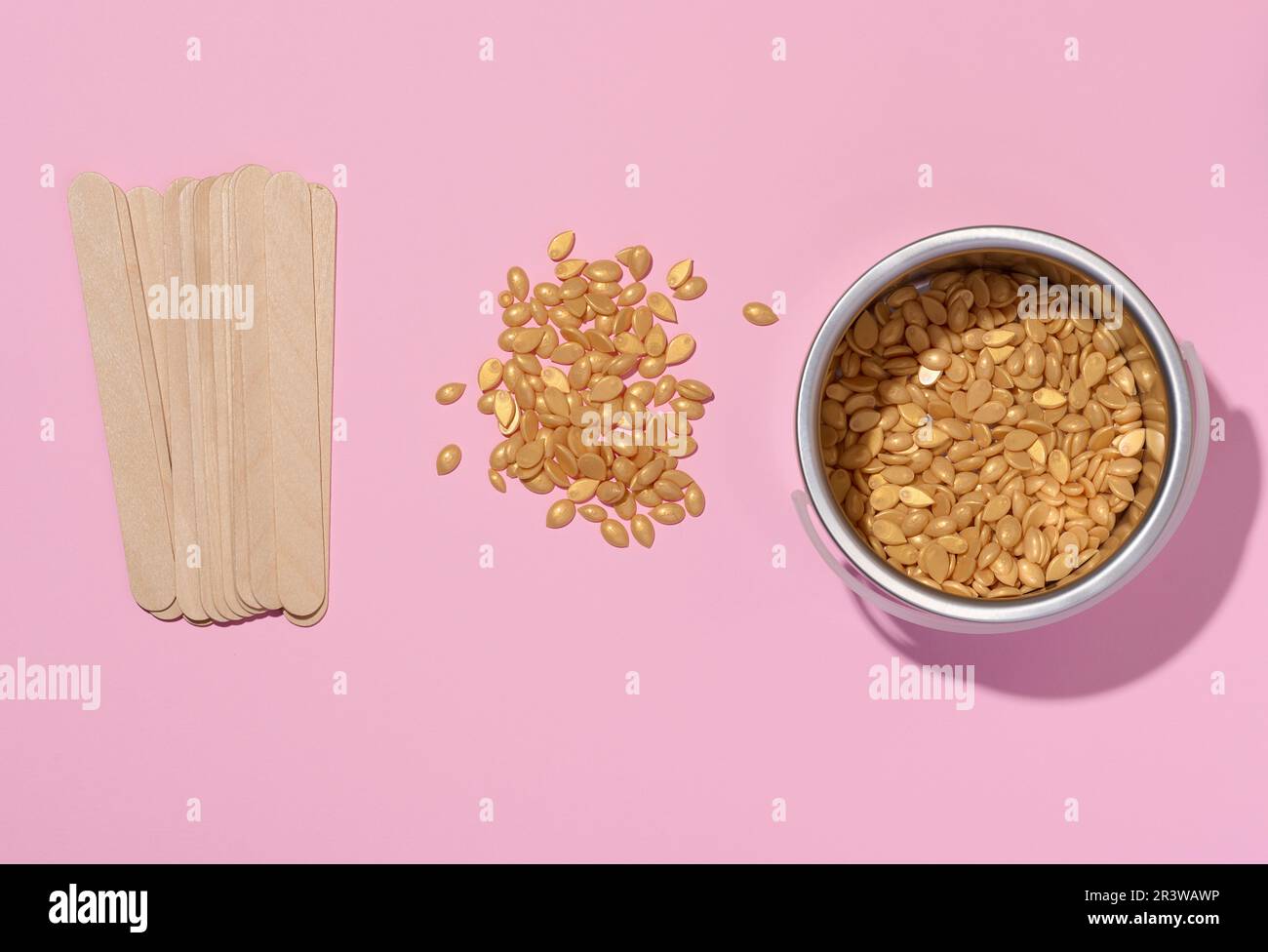 Bastoncini di legno per l'applicazione di cera e granuli di cera gialla per procedure cosmetiche su sfondo rosa, vista dall'alto Foto Stock