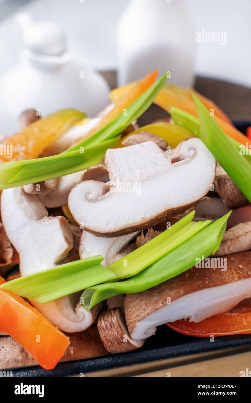 Funghi shiitake con verdure surgelate, peperoni, cipolle e pomodori sono pronti per la cottura. Piatto vegetariano di verdure con funghi shiitake. Foto Stock