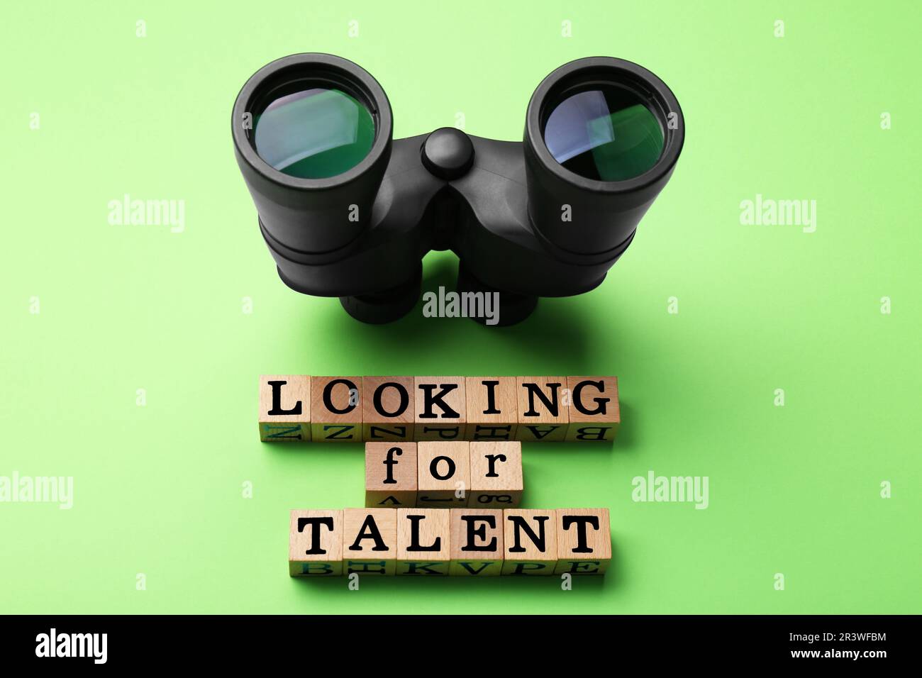 Concetto di reclutamento del personale. Frase cercando talento fatto di cubetti di legno e binocolo su sfondo verde chiaro, vista dall'alto Foto Stock