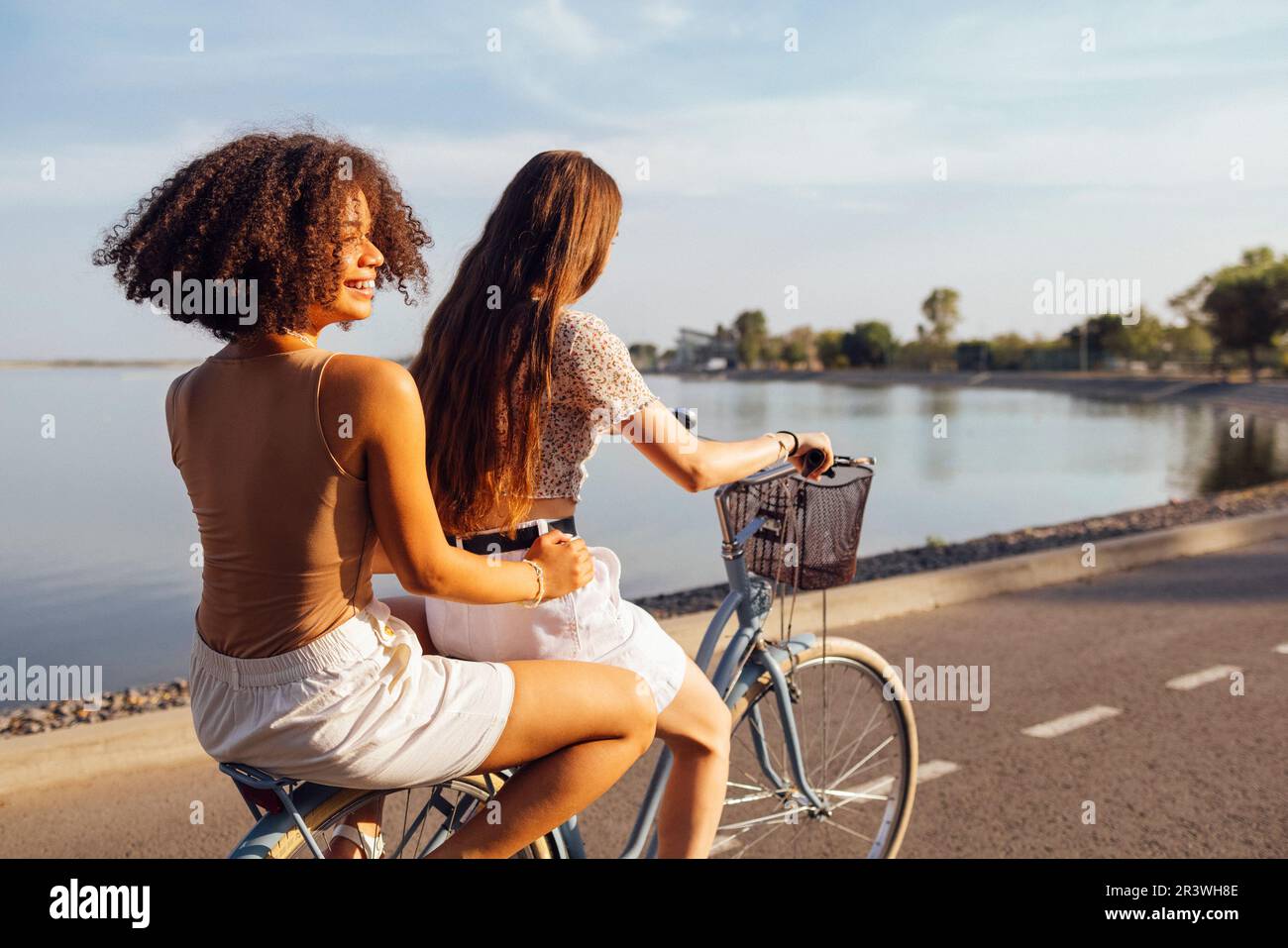 Adolescenti di diverse nazionalità e aspetto in bicicletta percorrono una strada cittadina. Le ragazze giovani e positive sorridono insieme Foto Stock