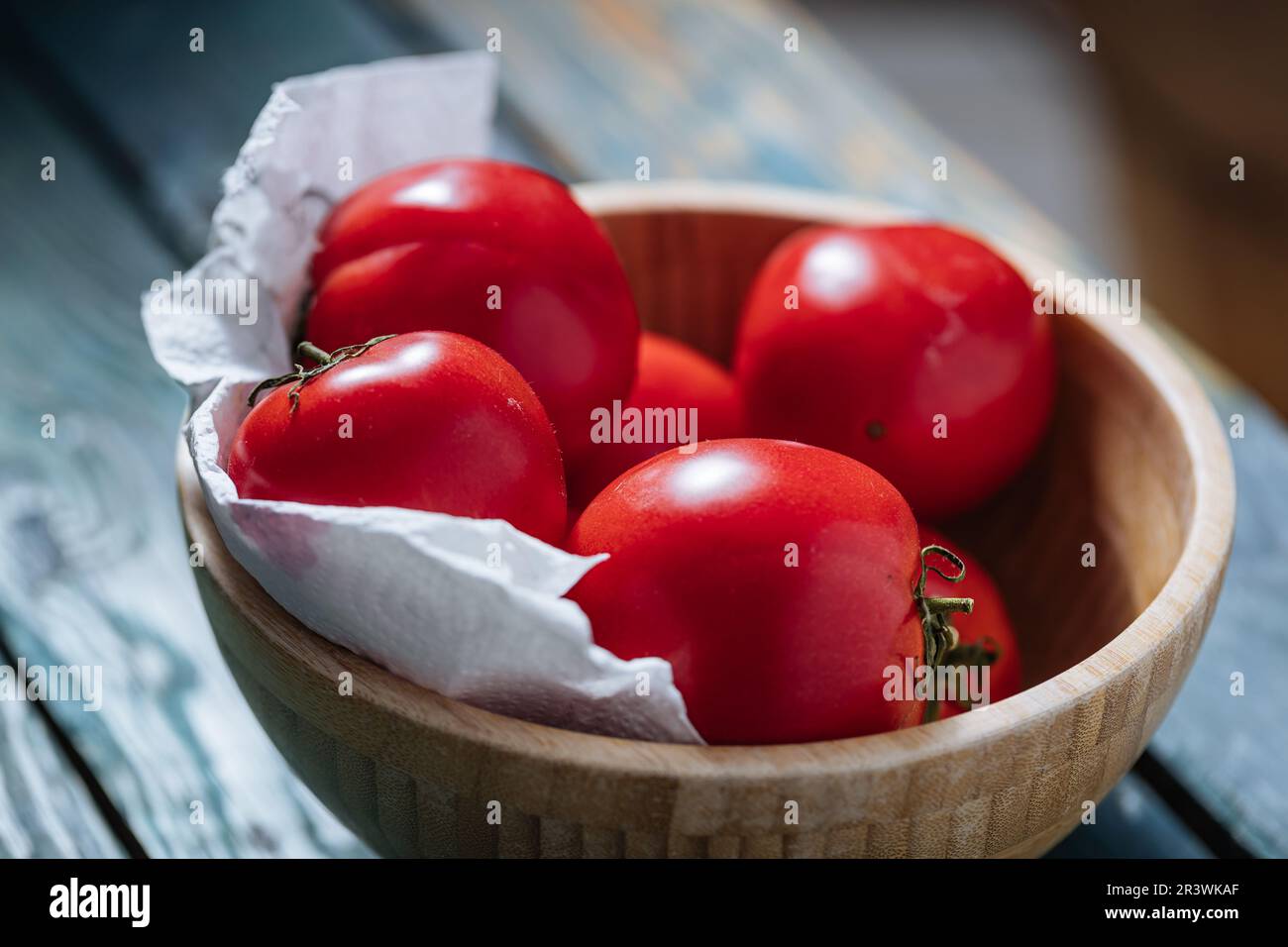 Una ciotola singola di pomodori freschi su tavola di legno blu in luce drammatica. scena minima Foto Stock