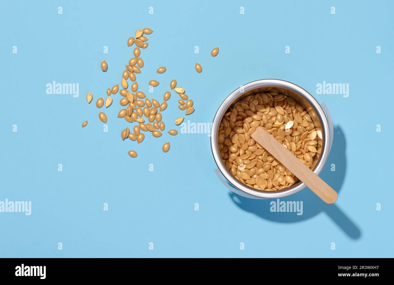 Bastoncini di legno per l'applicazione di cera e granuli di cera gialla per procedure cosmetiche su sfondo blu, vista dall'alto Foto Stock