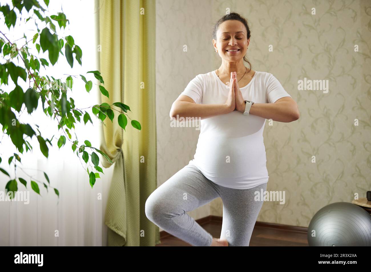 Vera donna incinta cosciente con gli occhi chiusi, pratica la gravidanza yoga in postura albero con le mani namaste gesto Foto Stock