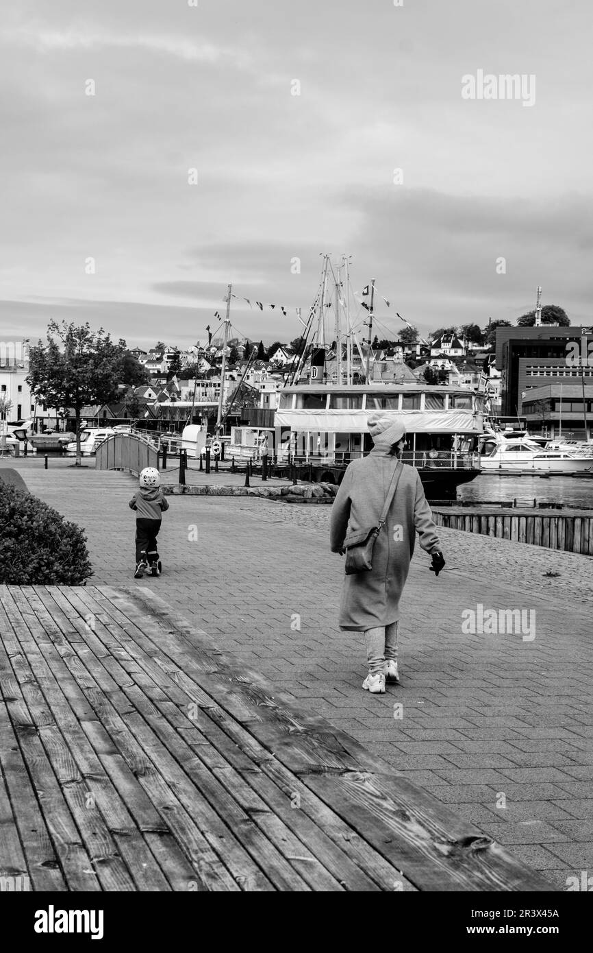 Sandnes, Norvegia, 18 2023 maggio, madre e bambino camminando da soli lungo il lungomare di Sandnes Harbour con barche da diporto sullo sfondo Foto Stock