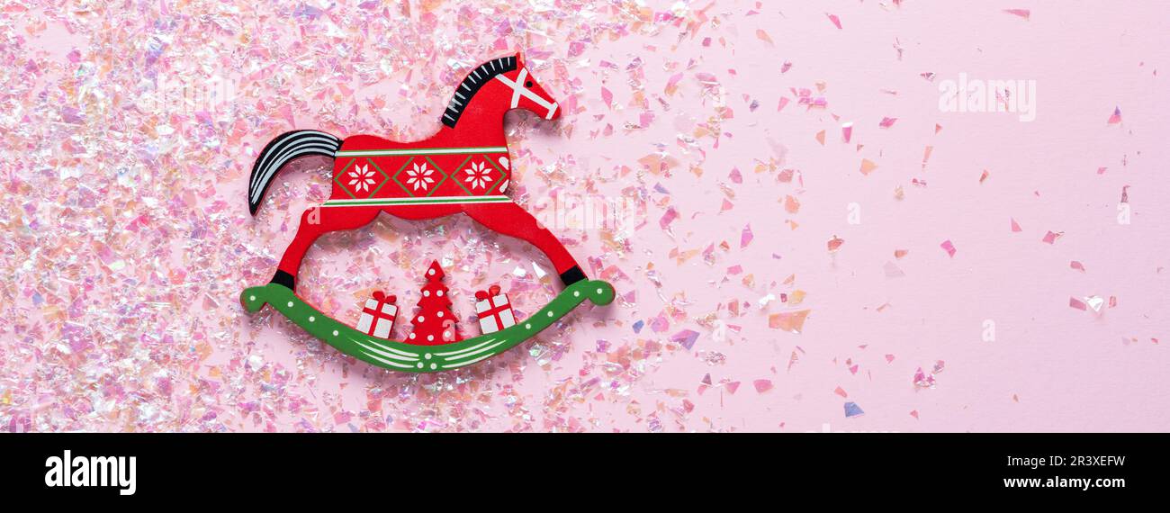 Giocattolo di Natale di cavallo dondolo su sfondo rosa con glitter. posa piatta Foto Stock