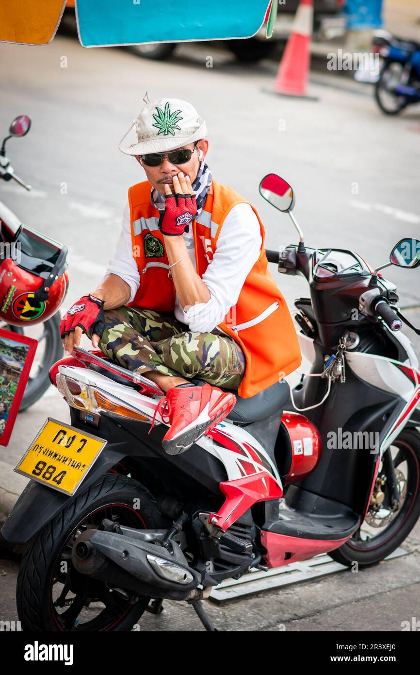Un motociclista thailandese molto bello che lavora come un servizio taxi prende una pausa seduto nella sua bicicletta a Pattaya Thailandia. Foto Stock