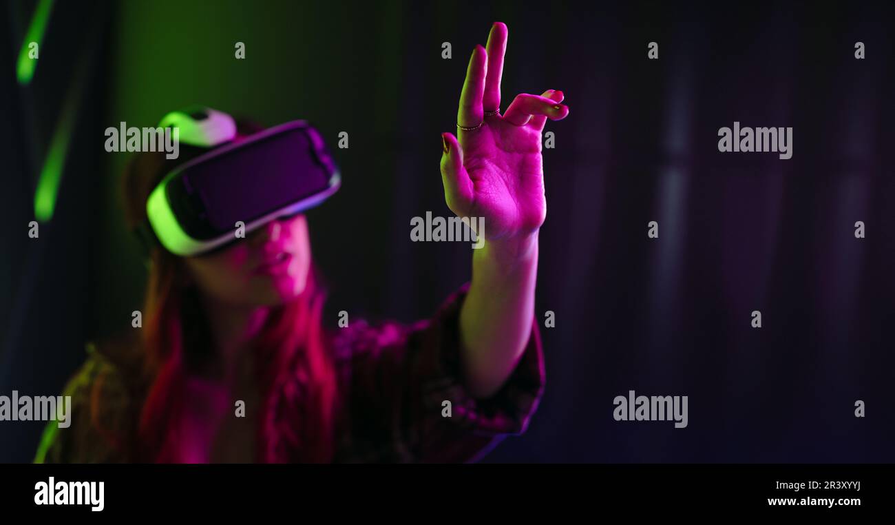 Indossando un visore VR, una giovane donna interagisce con oggetti digitali utilizzando i movimenti delle mani. Donna nel suo 20's esplorare la realtà virtuale, sperimentare al Foto Stock