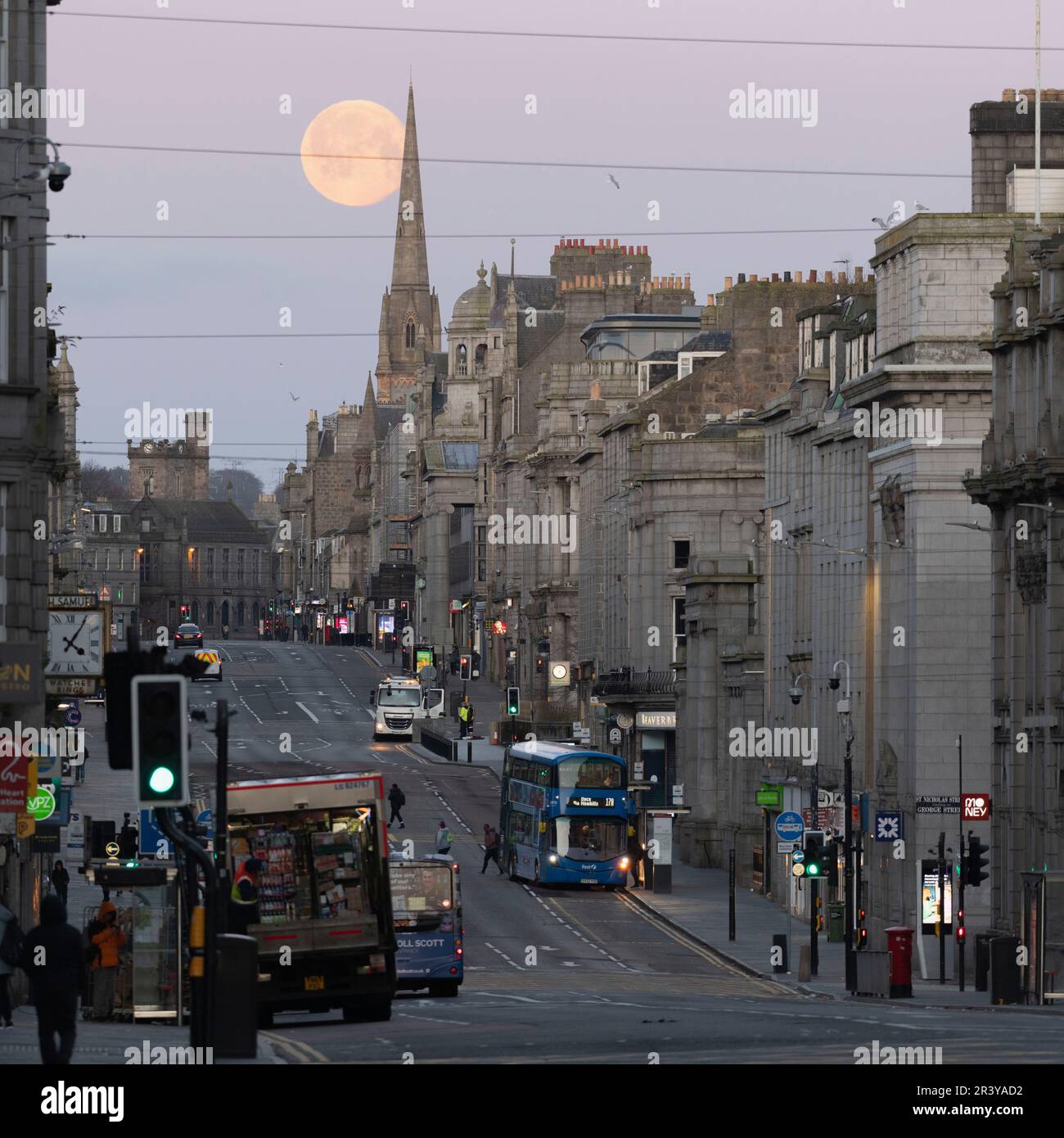 Guardando verso il West End di Union Street nel centro di Aberdeen come la Luna piena (rosa) si trova dietro Gilcomston Church spire poco prima dell'alba Foto Stock