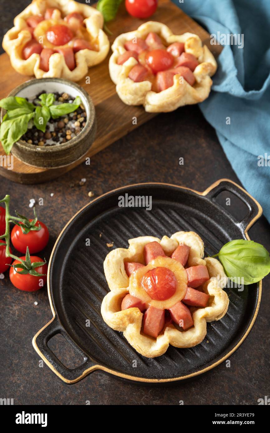 Mini pizza, colazione. Pizza in pasta sfoglia con formaggio e pomodori su un tavolo di pietra. Foto Stock