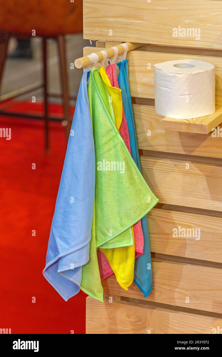 Molti vestiti colorati in microfibra appesi e rotolo di carta igienica a cabina bagno con scaffale di legno Foto Stock