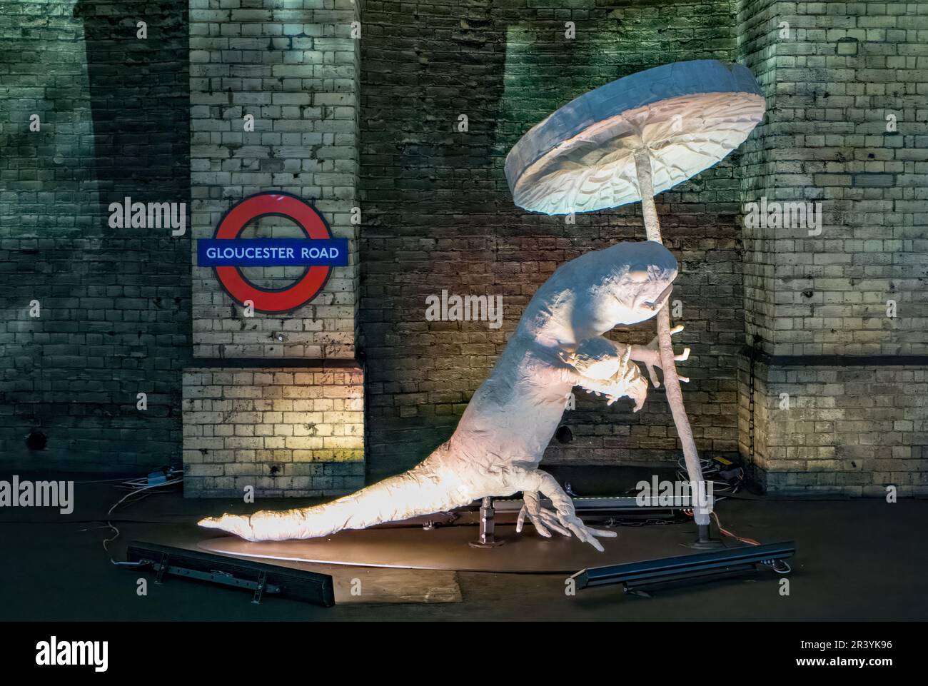 Un grande modello di salamandra bianca che tiene un giglio gigante su una piattaforma in disuso alla stazione della metropolitana di Gloucester Road a Londra, Regno Unito. Questo fiorma parte del Foto Stock