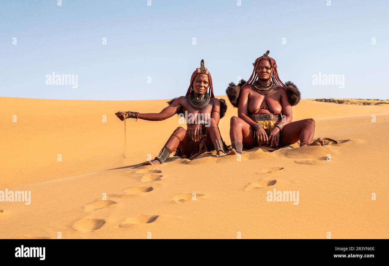 Due donne Himba sono sedute sulla sabbia nel deserto. Foto Stock