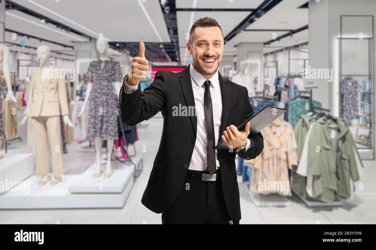 Uomo d'affari con appunti e documenti che mostrano pollici all'interno di un negozio di abbigliamento Foto Stock