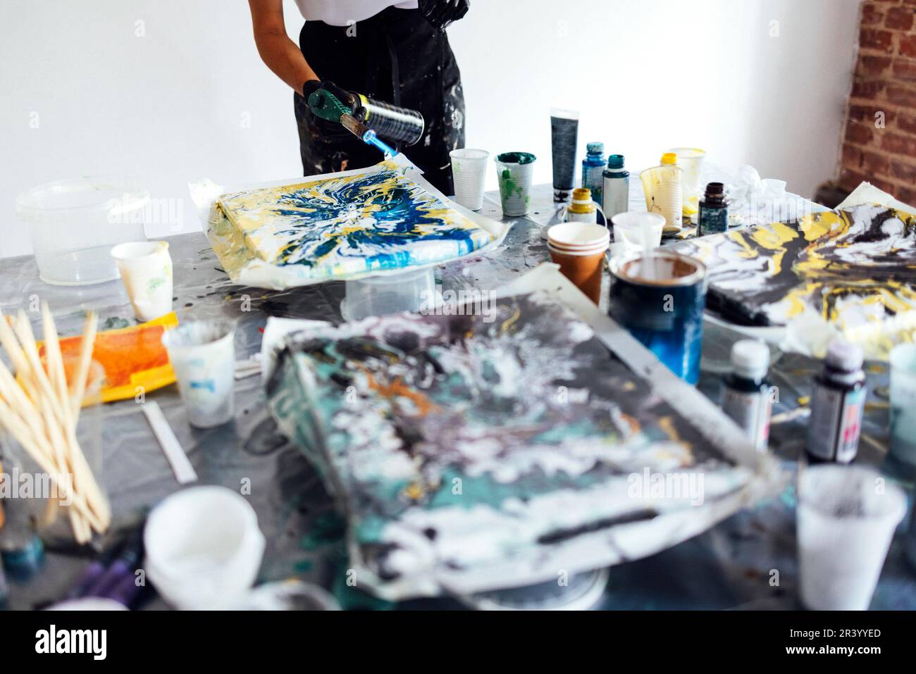 Donna utilizza un bruciatore a gas per disegnare in fluido Art. Processo di creazione di una pittura con vernici acriliche liquide. Foto Stock