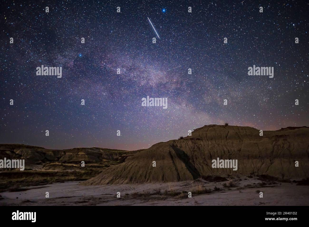 Un treno di satelliti Starlink che si spostano verso est sul paesaggio illuminato dalla luna del Dinosaur Provincial Park, Alberta Canada. Foto Stock