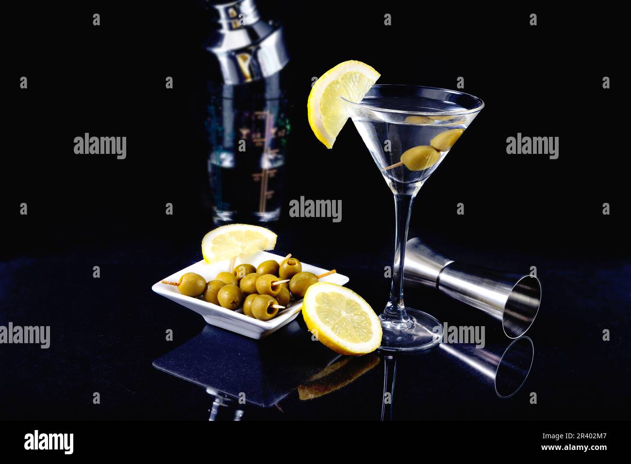 Bicchiere di cocktail martini secchi con olive e limone con piatto di olive su sfondo nero, fotografia scura Foto Stock