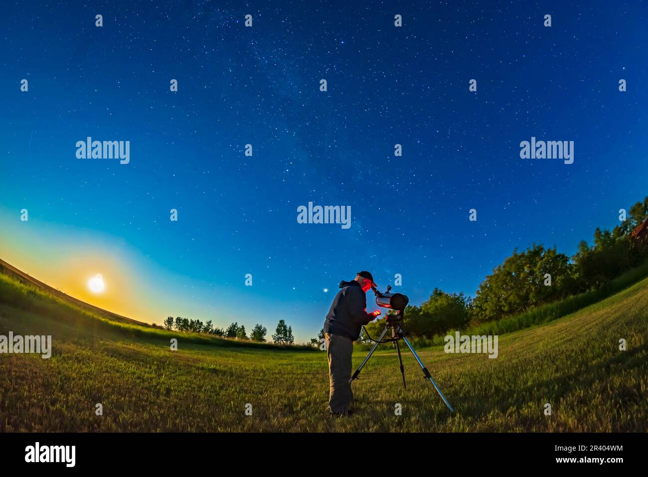 Astronomo che usa un telescopio nel cortile posteriore in una notte di luna luminosa, con la luna gibbosa in declino che si alza a sinistra. Foto Stock
