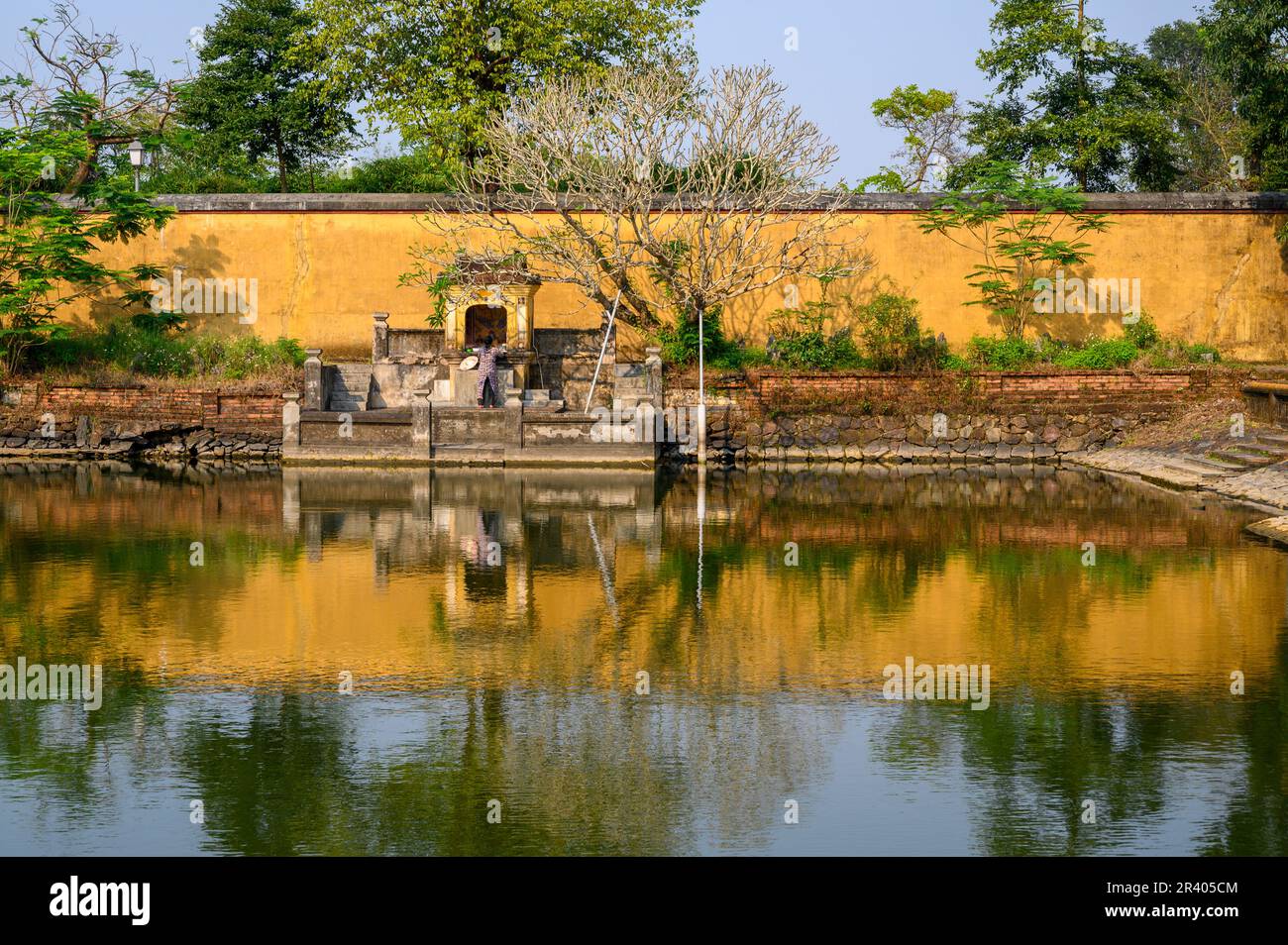 Un muro giallo, alberi e un santuario che si riflette su uno stagno nella città imperiale, Cittadella di Hue, l'antica capitale del Vietnam. Foto Stock