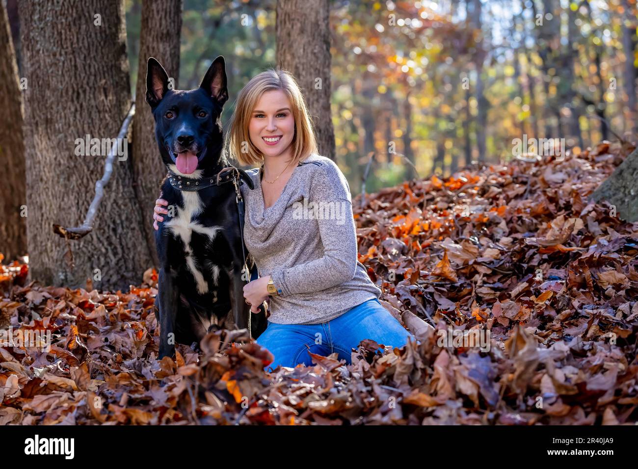 Una bella modella bionda si posa all'aperto mentre si gode il clima autunnale con il suo cane da compagnia in Un parco Foto Stock