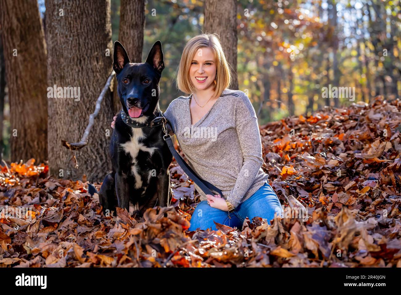 Una bella modella bionda si posa all'aperto mentre si gode il clima autunnale con il suo cane da compagnia in Un parco Foto Stock