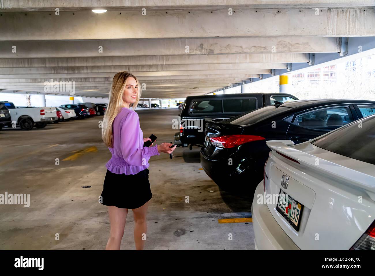 Una bella Blonde Executive Assistant cammina verso la sua auto in Un ponte di parcheggio coperto dopo Una lunga giornata Foto Stock