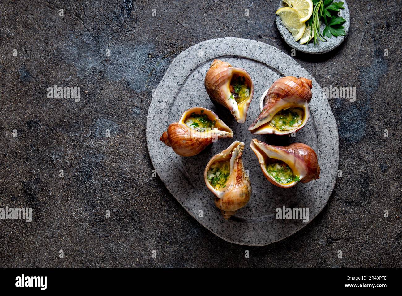 Cileno lumache giganti con burro e aglio ed erbe sulla pietra grigia piastra. escargot dall'oceano pacifico Foto Stock