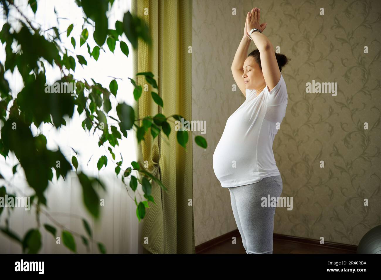 Ritratto laterale di autentica donna incinta attiva cosciente che pratica surya namaskar durante la gravidanza. Stile di vita sano Foto Stock