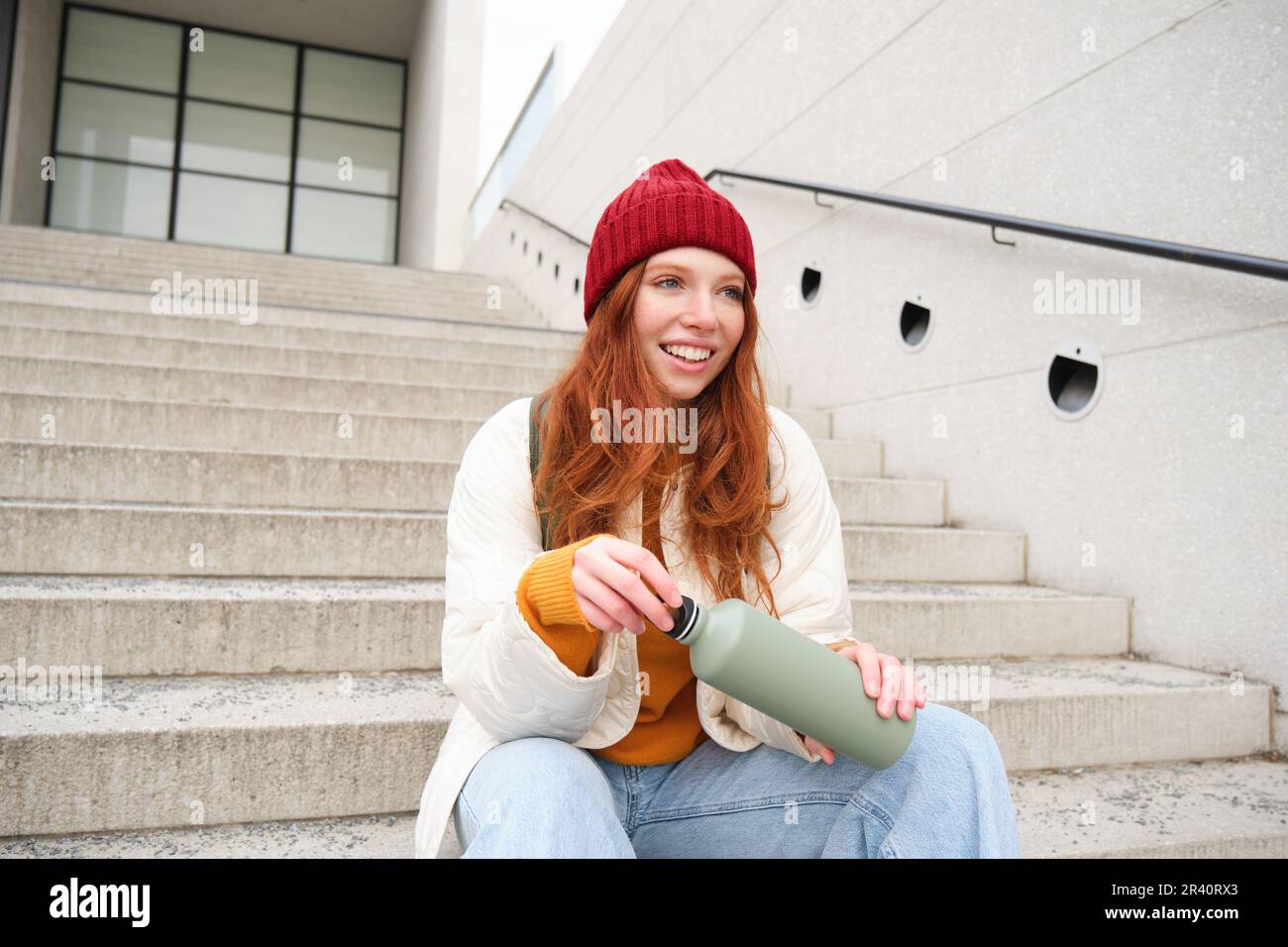 Un viaggiatore sorridente, una ragazza rossa che si siede sulle scale con  una borraccia, beve un caffè caldo dai thermos mentre viaggia e visita la  città Foto stock - Alamy