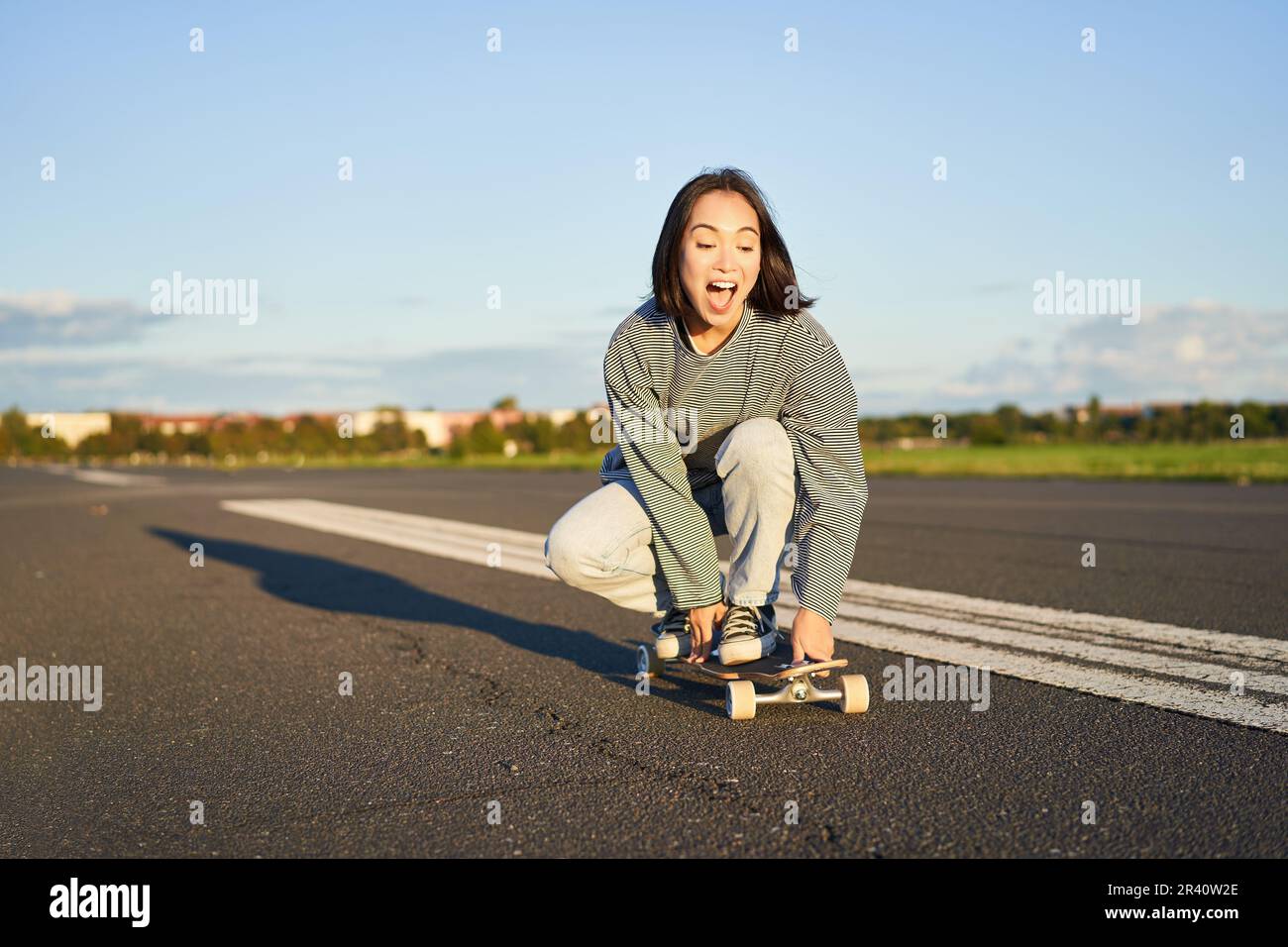 Ritratto di spensierata, felice ragazza asiatica pattinaggio, equitazione skateboard e ridere, godendo di una giornata di sole Foto Stock