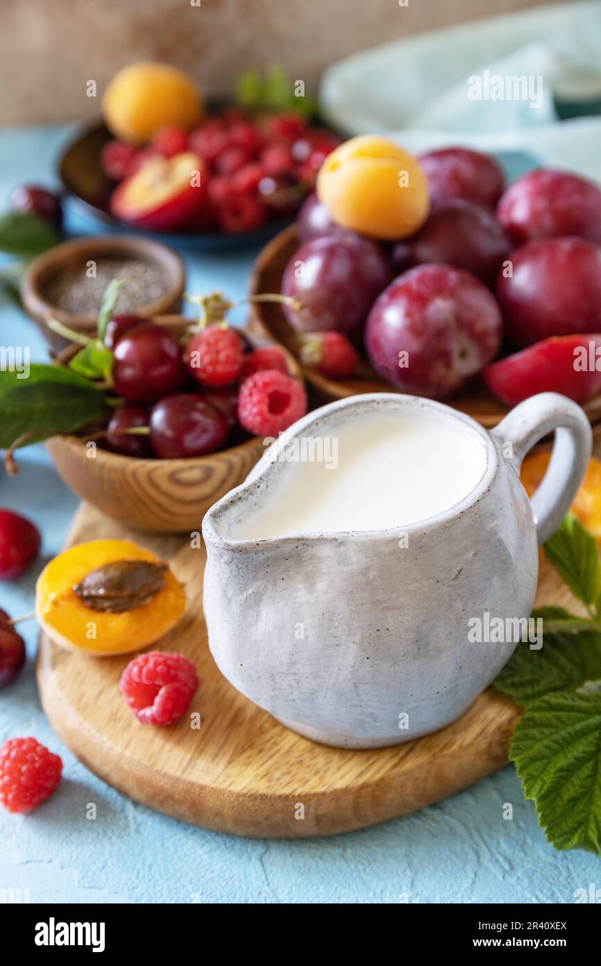 Ingredienti per un frullato sano. Latte e frutti di bosco (lampone, ciliegia, prugna, albicocca) su un piano di pietra. Mangiare sano, crudo Foto Stock
