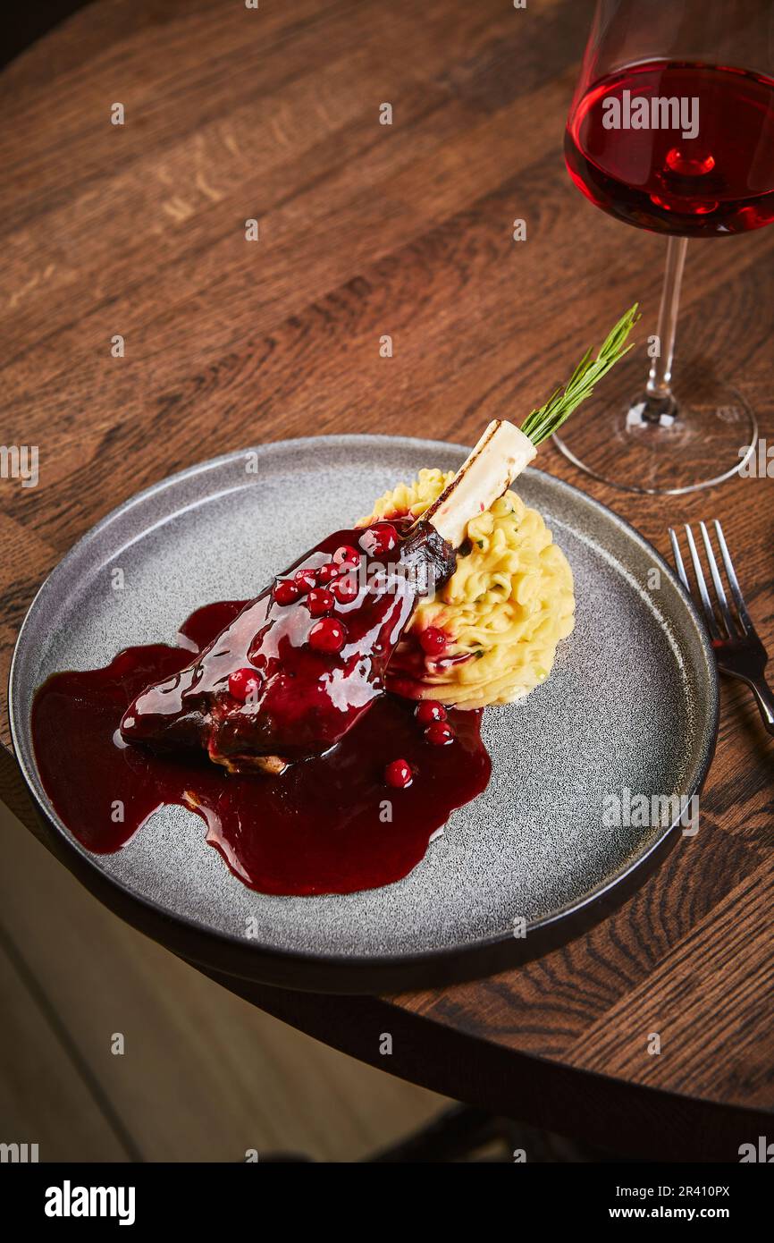 Coscia di agnello con salsa di mirtilli rossi o mirtilli rossi e purè di patate. Un bicchiere di vino, piatto di festa Foto Stock