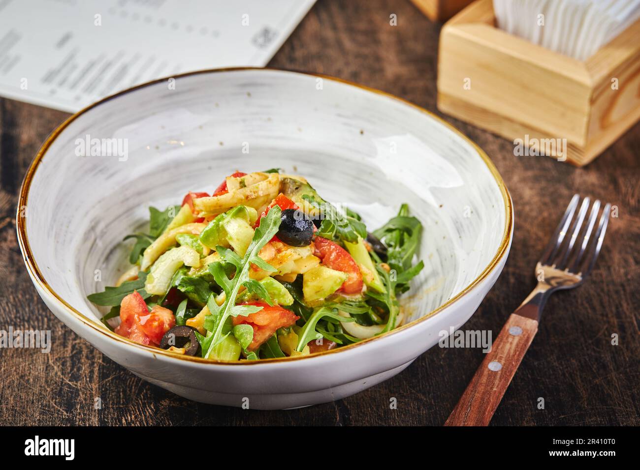 Insalata con calamari, rucola, sedano e avocado, pomodori e olive su piatto bianco su tavolo di legno Foto Stock
