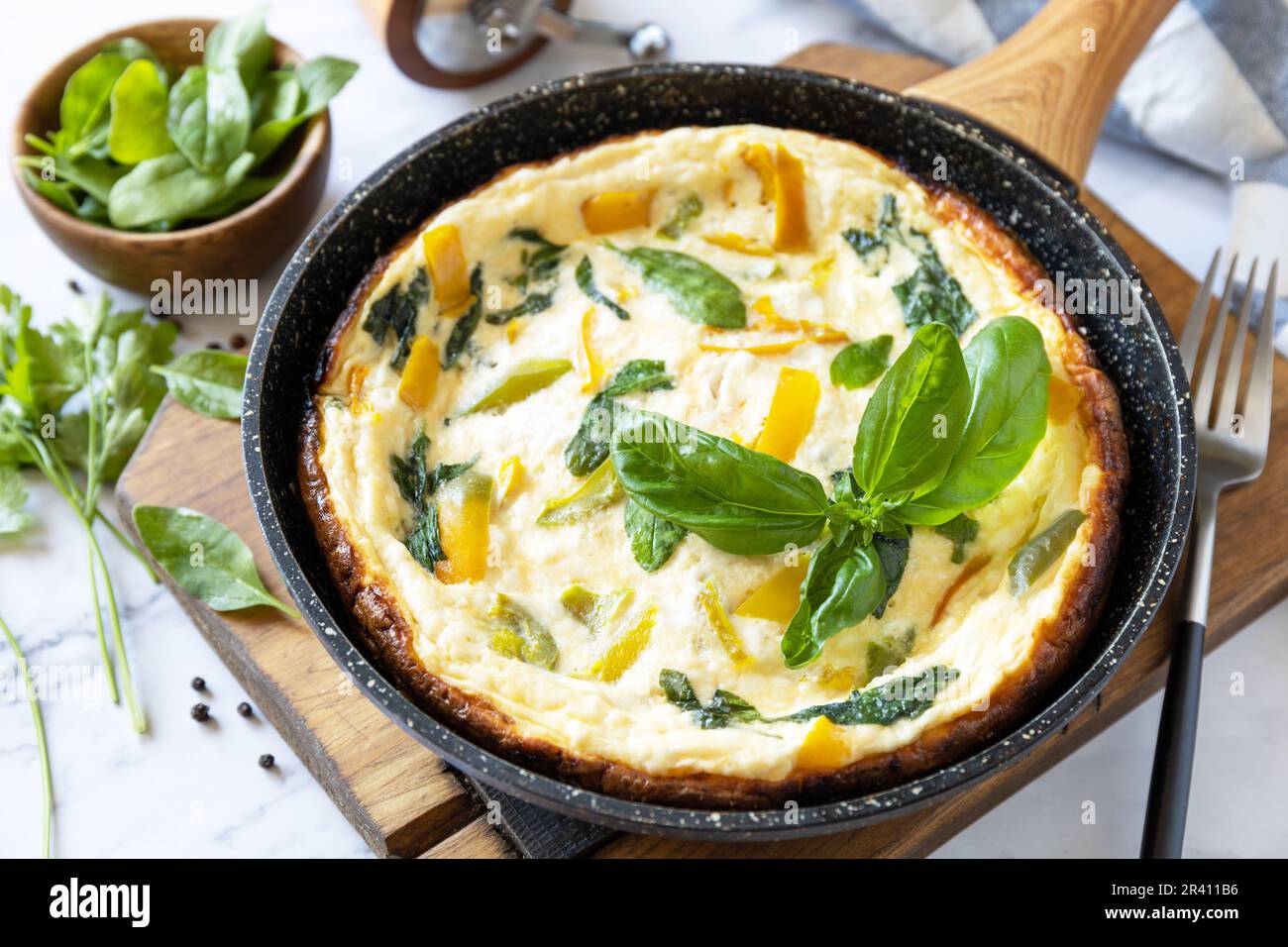 Spinaci e omelette al formaggio. Frittata di uova, paprika e spinaci in padella su un piano di marmo. Foto Stock