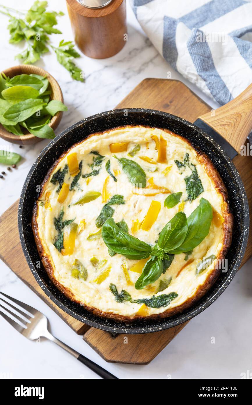 Spinaci e omelette al formaggio. Frittata di uova, paprika e spinaci in padella su un piano di marmo. Foto Stock