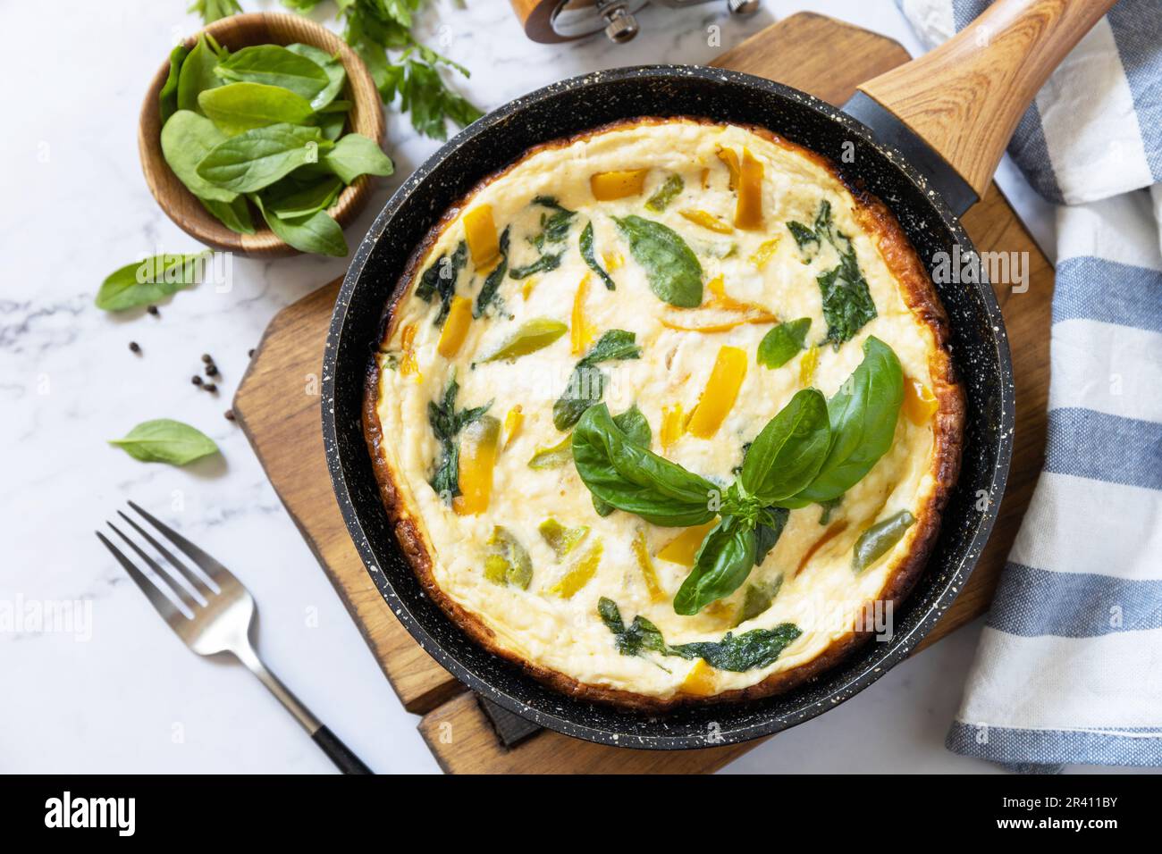 Spinaci e omelette al formaggio. Frittata di uova, paprika e spinaci in padella su un piano di marmo. Foto Stock