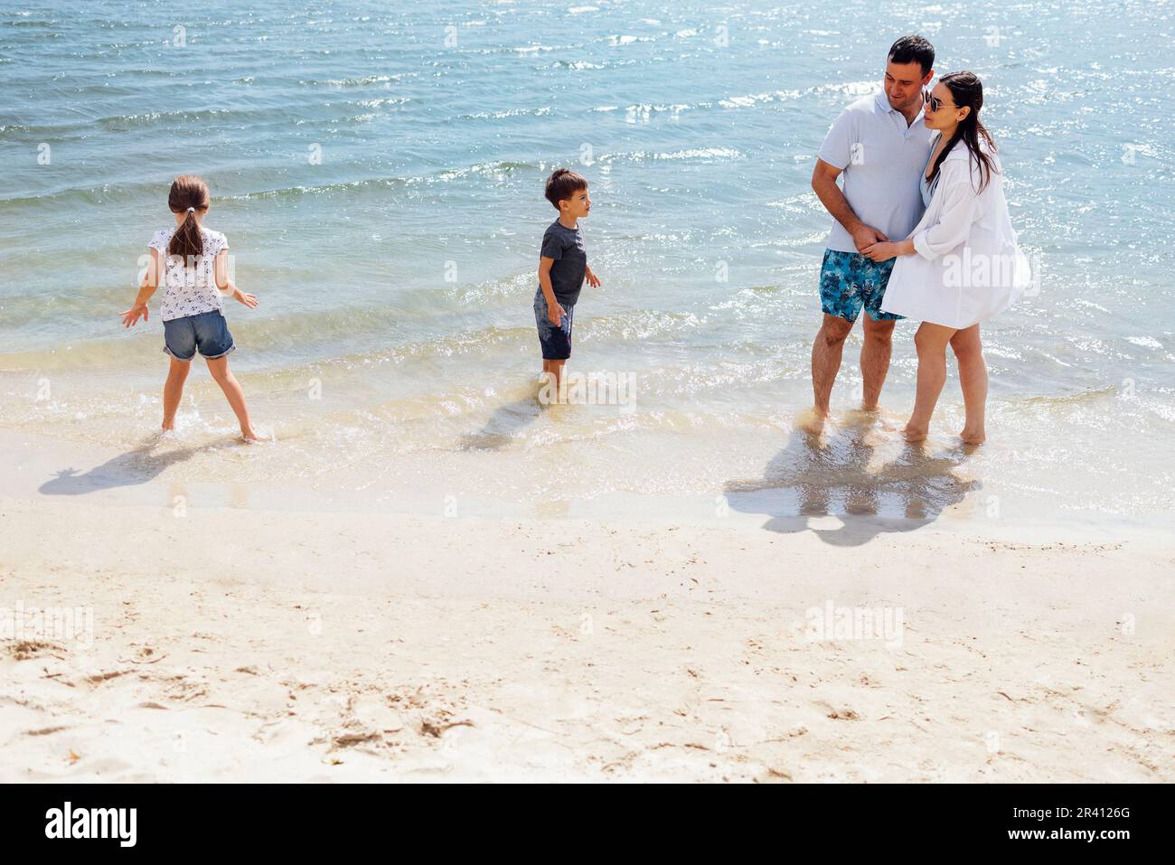 Figlio e figlia corrono sull'acqua e spruzzano sui loro genitori sorridenti Foto Stock