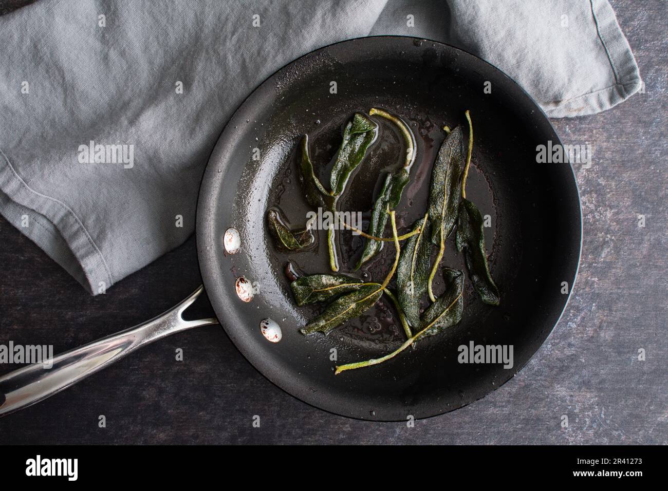 Foglie di salvia fritte in una padella non-Stick con burro: Vista dall'alto delle foglie di salvia fritte in una padella piccola Foto Stock