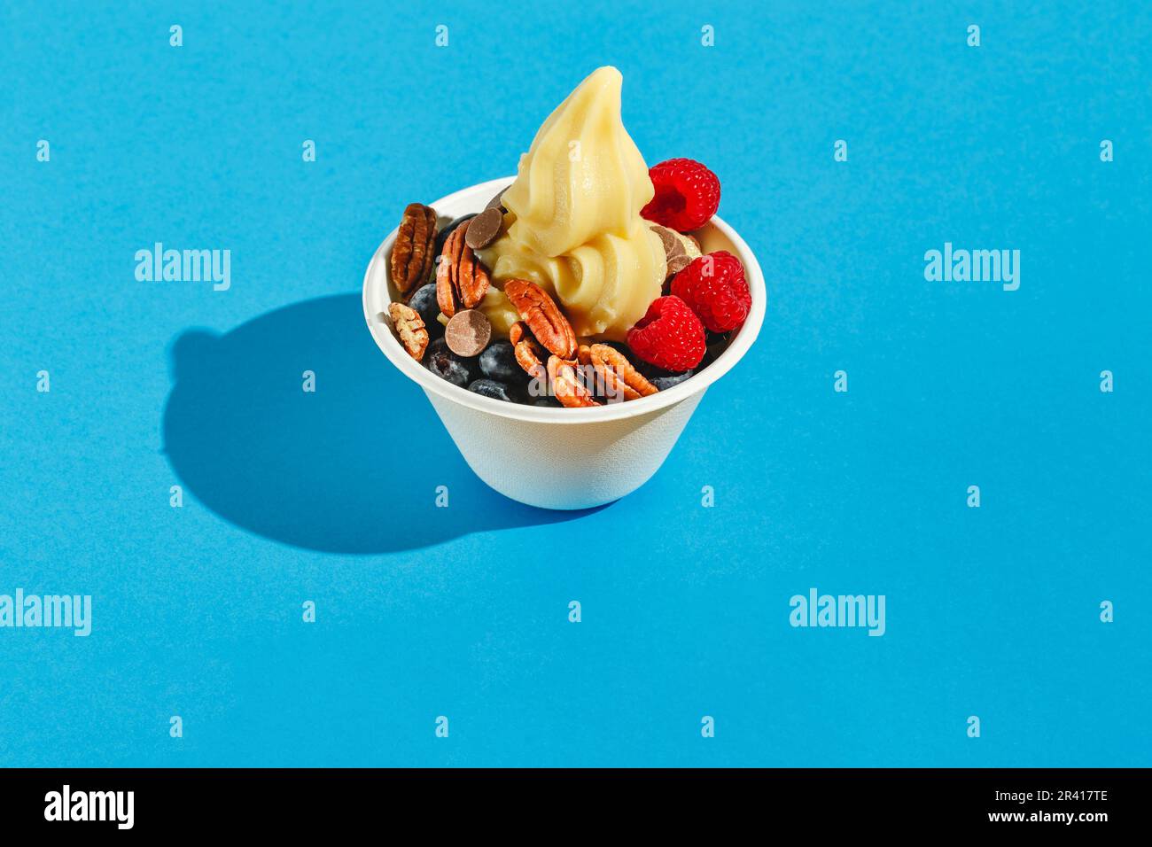 Yogurt congelato con lamponi, mirtilli, gocce di cioccolato e noci pecan. Luce dura, ombra profonda Foto Stock