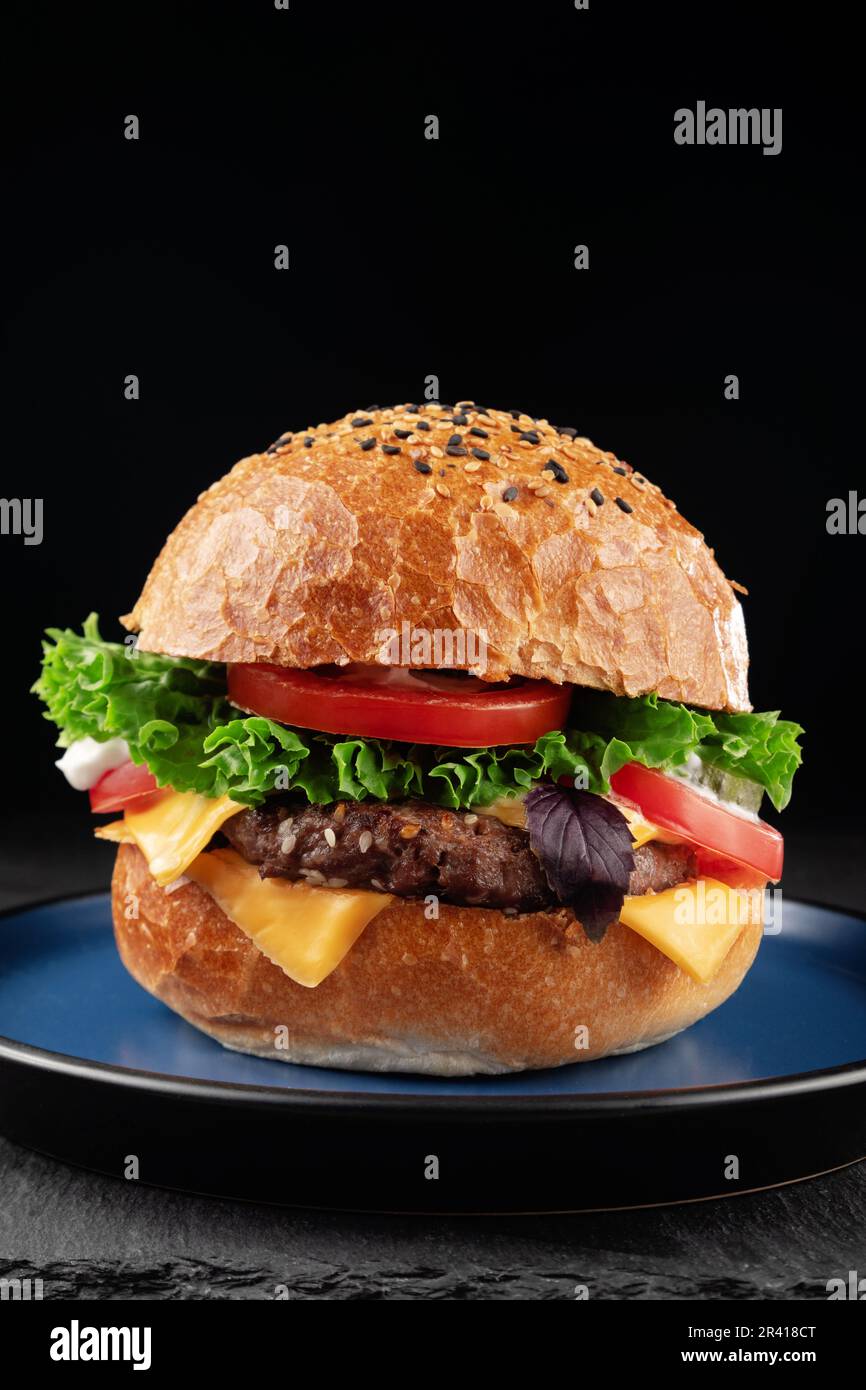 Hamburger con formaggio, lattuga e pomodoro su sfondo nero. Foto Stock