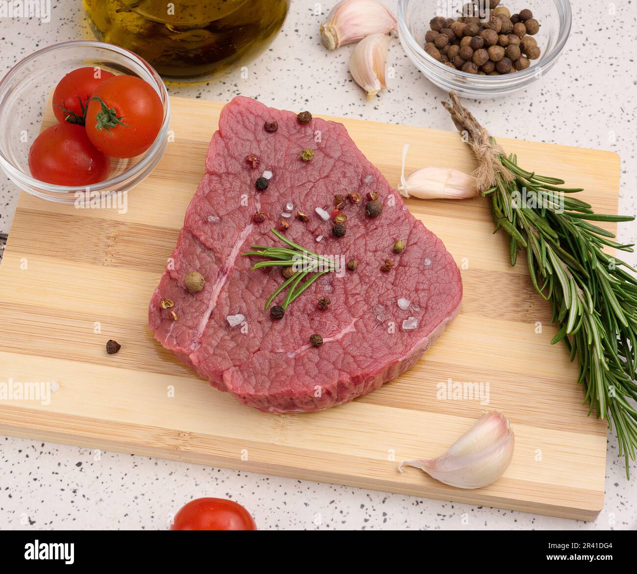 Pezzo di manzo crudo con spezie, pepe, rametto di rosmarino, sale e olio d'oliva su un asse di legno, vista dall'alto Foto Stock