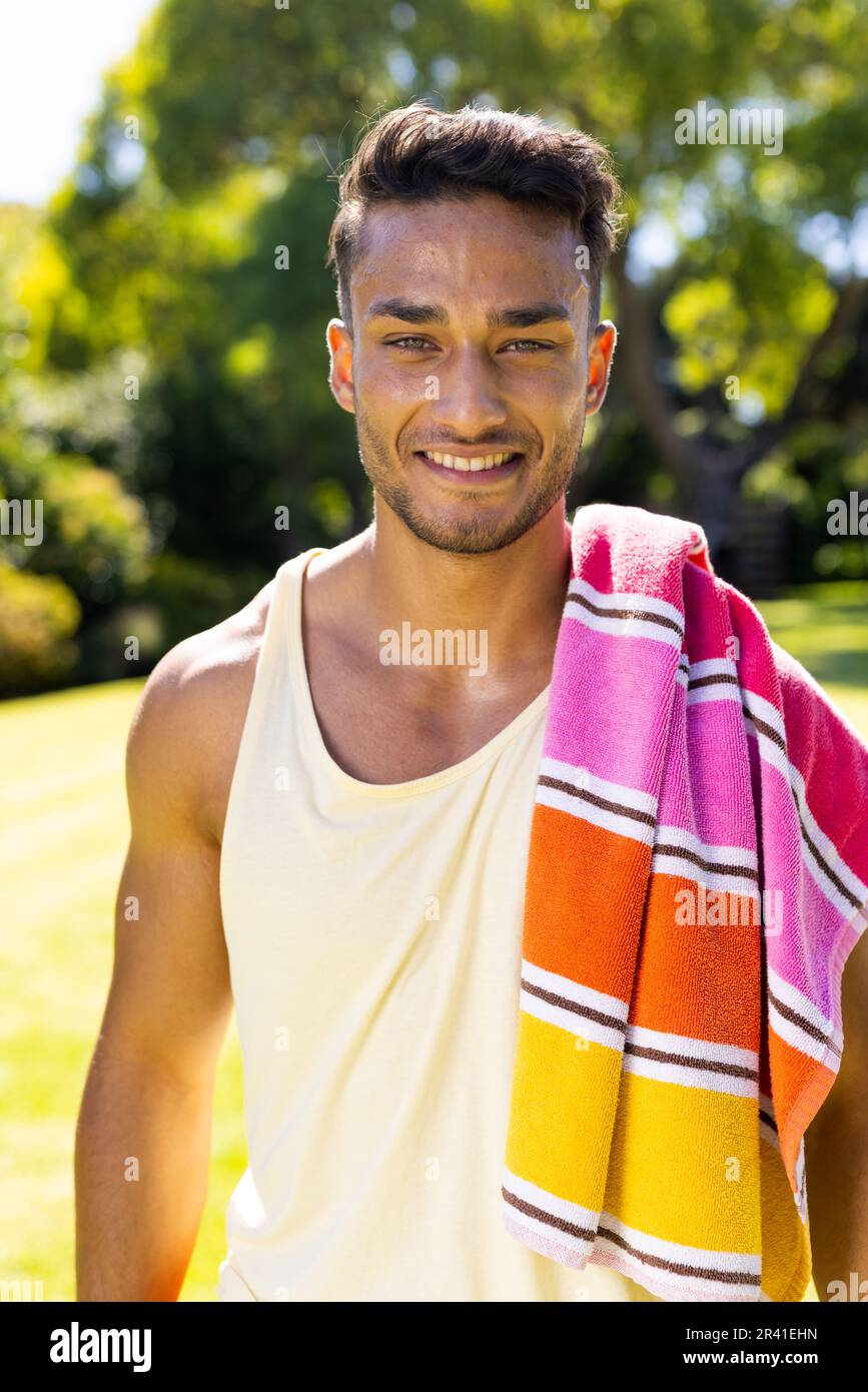 Ritratto di felice uomo biraciale con asciugamano sulla spalla guardando la macchina fotografica e sorridendo in giardino Foto Stock