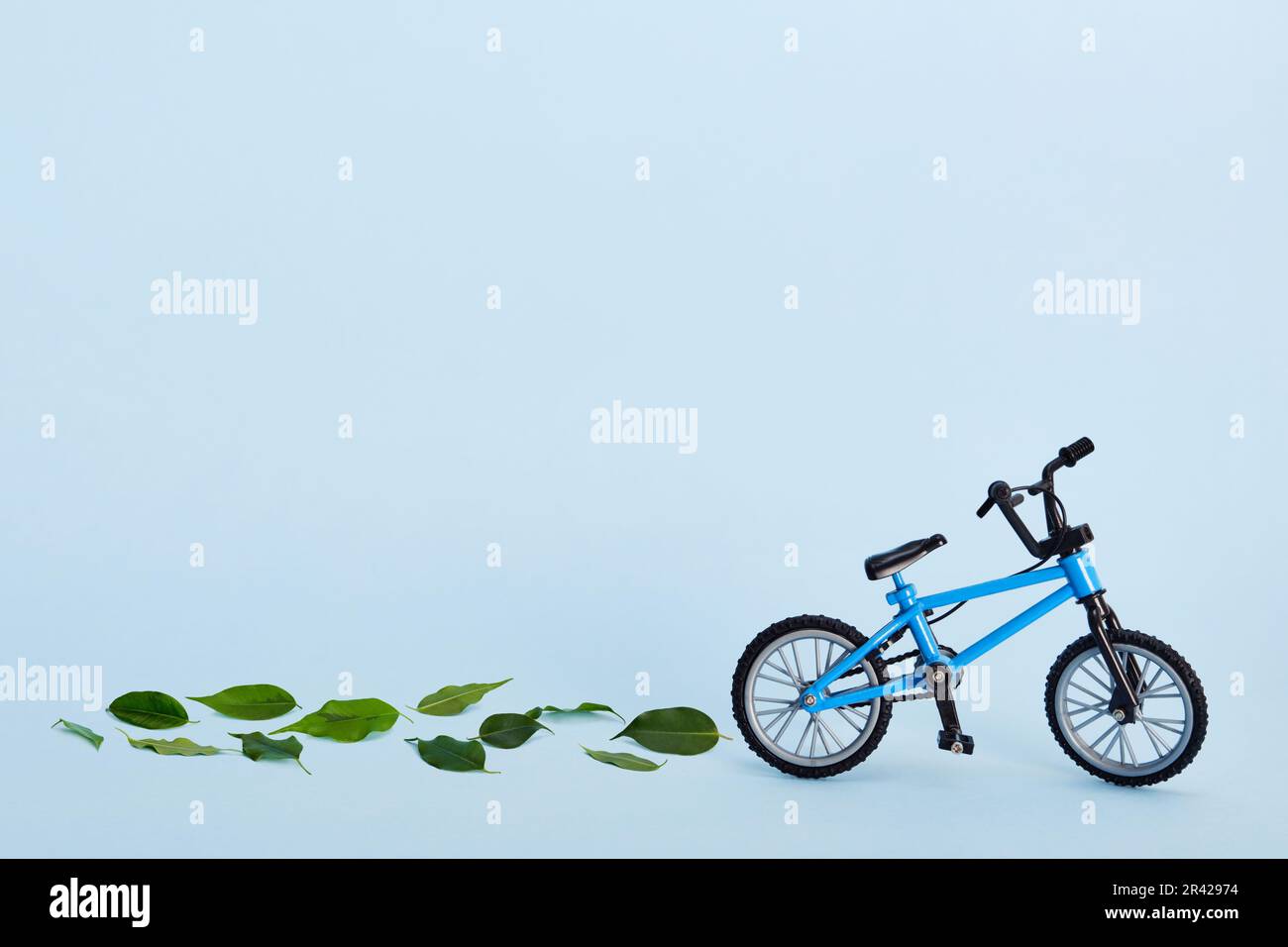 Giornata mondiale della bicicletta. Bicicletta e piste realizzate con foglie verdi fresche su sfondo blu. Concetto sostenibile e sano Foto Stock