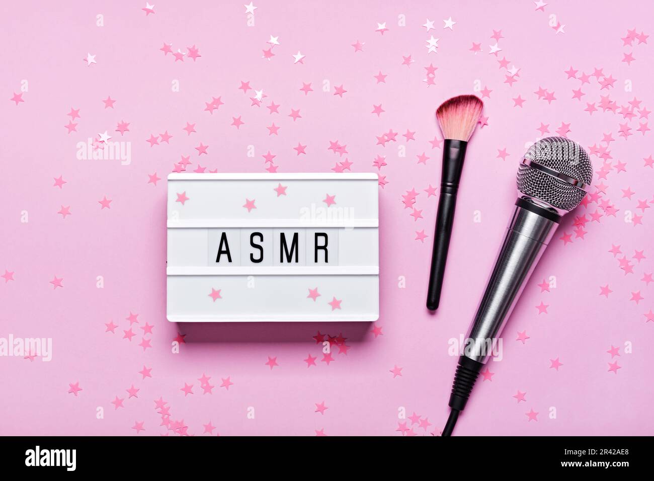 Microfono, pennello e scatola luminosa di testo ASMR su sfondo a cordonella rosa. ASMR registrazione concetto di stress alleviando i suoni, piatto, Foto Stock