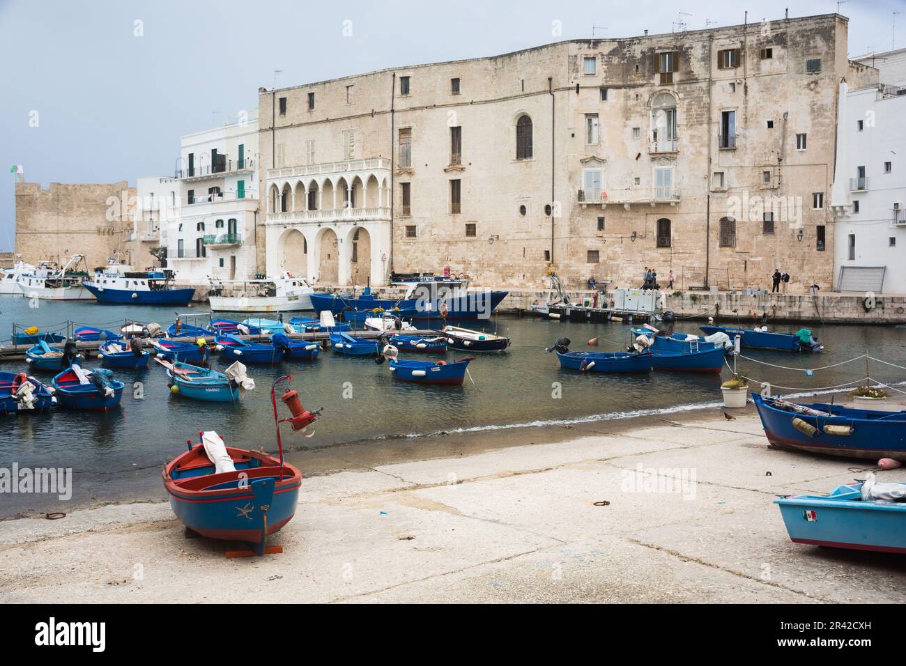 Barche di legno blu e rosse ormeggiate nel porto di Porto Antico, Monopoli, Puglia, Italia con antichi edifici storici in pietra bianca sullo sfondo. Foto Stock